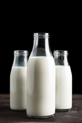 Three glass bottles with milk on a wooden table, black background