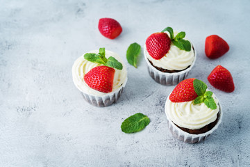 Chocolate cupcakes with cream cheese frosting, mint leaves and strawberries
