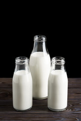 Three glass bottles with milk on a wooden table, black background