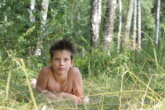 A brunette boy lies in the grass in a birch grove in the summer. Russian