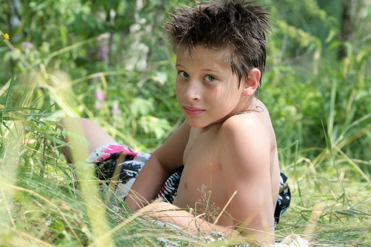 A brunette boy lies, sunbathes and looks over his shoulder in the grass in summer. Russian