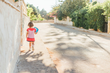 Fototapeta na wymiar girl holding a ball in her hands runs forward sunny street summer