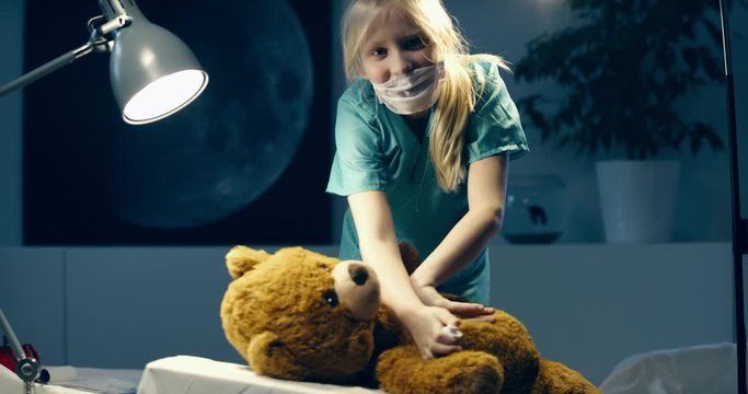 Cute little girl wearing doctor suit playing at home, pretending to be a surgeon, giving an injection to her teddy bear. Shot on RED Cinema camera with Cooke Prime lenses