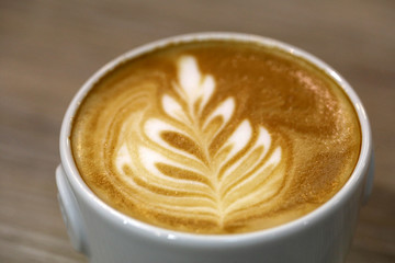 The coffee barista poured milk into the coffee and created a beautiful leaf.