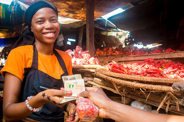 young african woman selling tomatoes in a local african market collecting money from a paying customer
