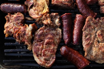 A barbecue where large pieces of meat and sausages are grilled.