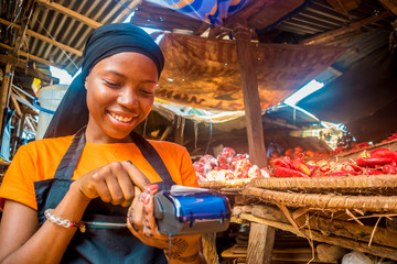 young african woman selling tomatoes in a local african market using her mobile pos device