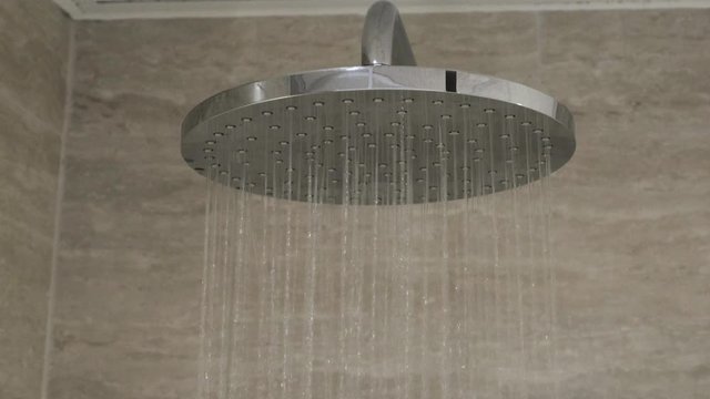 Close up view of water running in shower. Modern big round contemporary rain chrome shower head.