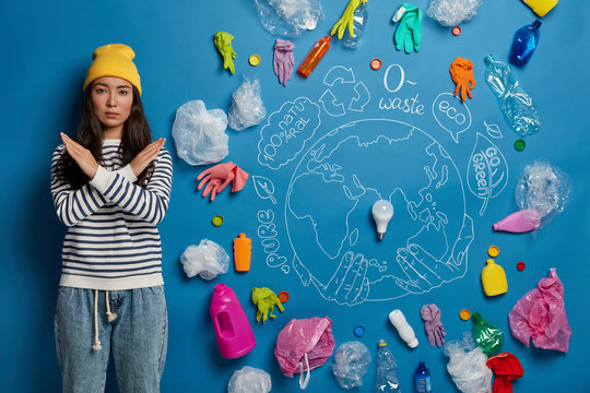 Ecology, plastic trash and environmental problems concept. Serious Asian woman crosses hands over chest, makes denial gesture, stands near dirty place with much litter around. Earth protection
