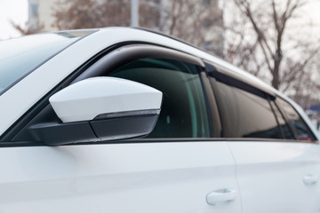 Close-up of the side left mirror and window of the car body white SUV on the street parking after washing and detailing in auto service industry. Road safety while driving