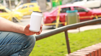 Hombre sosteniendo lata blanca con su mano, en un parque.