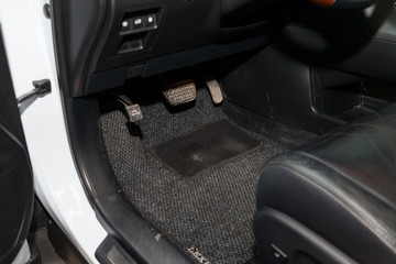 Dirty car floor mats of gray carpet with gas pedals and brakes in the workshop for the detailing...