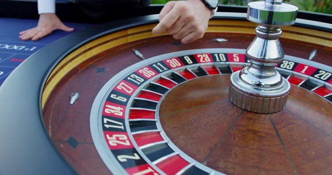 Man starts to spin the roulette wheel, as he throws the ball in circular motion stopping on number 8.