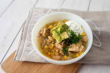 Flavorful White Chicken Chili made with hearty beans, tender chicken, and a rich and creamy broth in slow cooker, garnished with sour cream and avacado