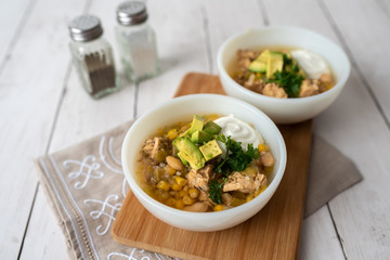 Flavorful White Chicken Chili made with hearty beans, tender chicken, and a rich and creamy broth in slow cooker, garnished with sour cream and avacado