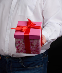 adult man in a white shirt holds a pink gift cardboard box with a bow