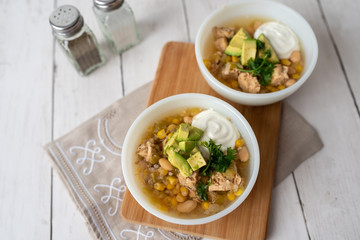 Flavorful White Chicken Chili made with hearty beans, tender chicken, and a rich and creamy broth in slow cooker, garnished with sour cream and avacado