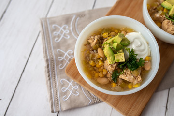 Flavorful White Chicken Chili made with hearty beans, tender chicken, and a rich and creamy broth in slow cooker, garnished with sour cream and avacado