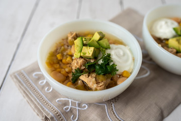 Flavorful White Chicken Chili made with hearty beans, tender chicken, and a rich and creamy broth in slow cooker, garnished with sour cream and avacado
