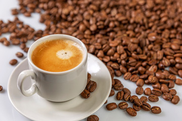 A small white cup of coffee stands on coffee beans. Fragrant pleasure. Space for text. White background.