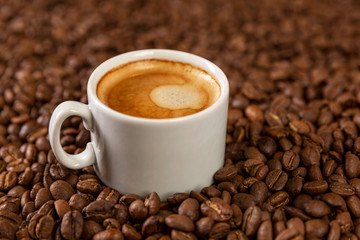 A small white cup of coffee stands on coffee beans. Fragrant pleasure. Background. Space for text.
