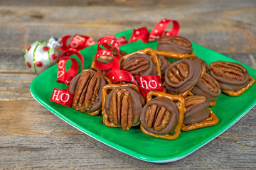 chocolate candy melted on salty pretzels with red Christmas ribbon and ornament on green square plate 