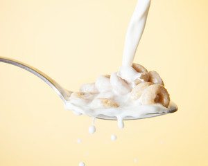 Cereal with milk pouring on top of it in a spoon against a yellow background