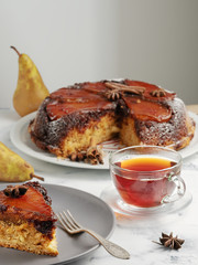Slice of homemade pie with ricotta and caramelized pear on a gray plate. Red tea in a glass mug next to the pie. Close-up.