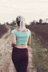 back of young woman in sportswear running distance in the field, girl engaged in sport outdoors on a cloudy day, concept healthy lifestyle and bodycare