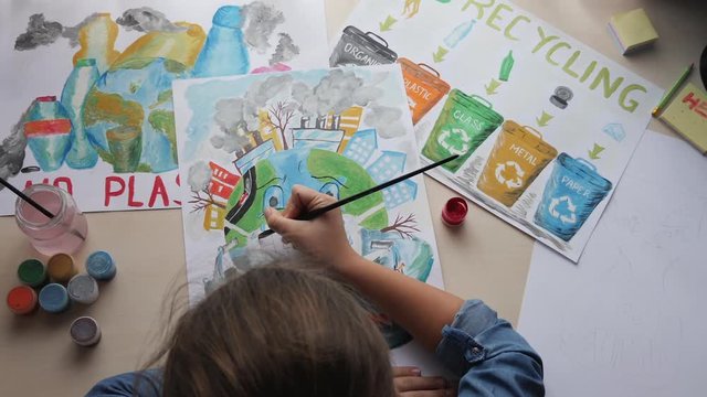 Top view of a girl paints posters calling to save planet Earth from pollution