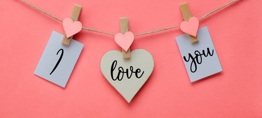 I love you - Clothes pegs with wooden hearts and paper notes hang on rope isolated on pink texture...