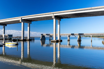 The calm waters and causeway bridge spanning Fancy Bluff Creek to Jekyll Island are seen from the marina. The Sidney Lanier Bridge into Brunswick is in the background. - obrazy, fototapety, plakaty