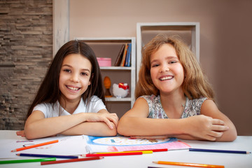 two beautiful teenage girls, a brunette and a blonde laugh, look forward and draw with colored...