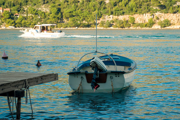 White and blue motor boat stands near the wooden pier on the background of passing by water taxi