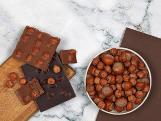 Broken chocolate bars and raw hazelnuts on gray marble background