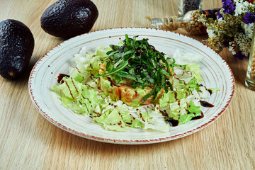 Tasty, fresh green salad with salmon, lettuce, avocado, parmesan on a white plate on a wooden background. Healthy diet