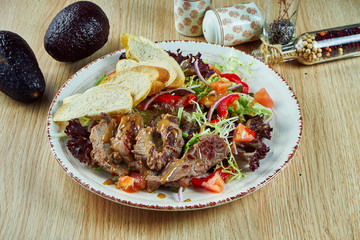 Juicy meat salad with baked veal vitello tonato, lettuce, onions and cherry tomatoes in a white bowl on a wooden background. Healthy food. Close up view