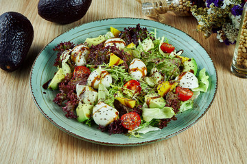 Juicy, green salad with farm mozzarella, lettuce, sesame seeds, avocado and cherry tomatoes in a blue bowl on a wooden background. Healthy food. Fitness nutrition. Tasty close up