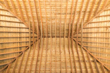 Looking directly up under a wooden roof, from inside. Beams and trusses visible.