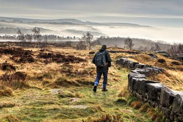 Stone wall and hiker leading into misty Derwent Valley landscape