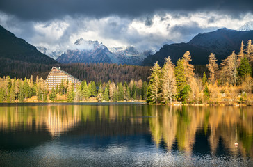 Tatra mountains in autumn. Lake Strbske pleso with lighted trees and mountains in clouds