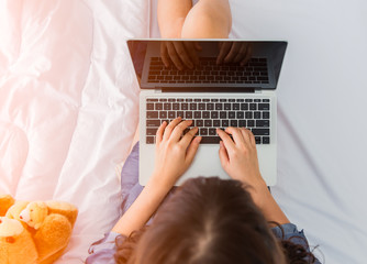 Young asian woman sitting on bed using laptop
