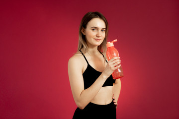 Young brunette girl in a black top with a bottle of water, posing on a red cherry background. Copy space