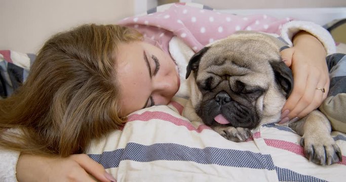 Adorable teen girl and her pug dog in the bed are sleeping together.  Friendship with pet concept. Together forever, inseparable friends