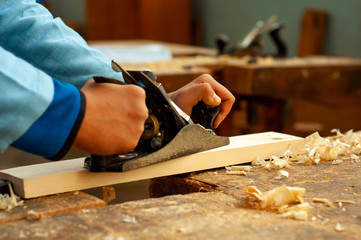 profession, people, carpentry, woodwork and people concept - carpenter working with jointer planing wood plank at workshop