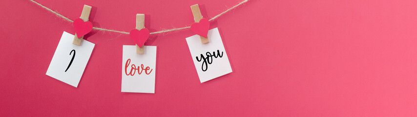 I love you - Clothes pegs with wooden hearts and paper notes hang on rope isolated on pink texture...
