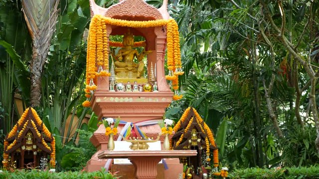 Wooden miniature guardian spirit house. Small buddhist temple shrine, colorful flower garlands. San phra phum erected to bring fortune. Traditional respect animistic rituals, pray ceremonies.