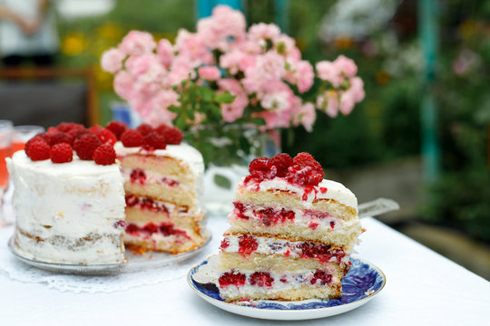 A slice of homemade raspberry cake on a saucer next to a cake on in the summer garden. Selective focus