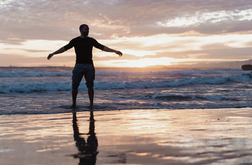 Hombre con camisa y pantalones recogidos caminado por la playa al atardecer	