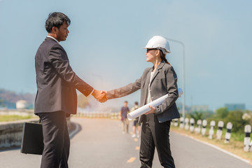 Asian woman engineers standing smiling hand holding blueprint and happy shaking hands to male businessman
